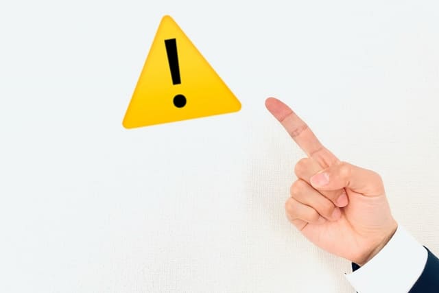 人が黄色い注意マークを指さしている画像
