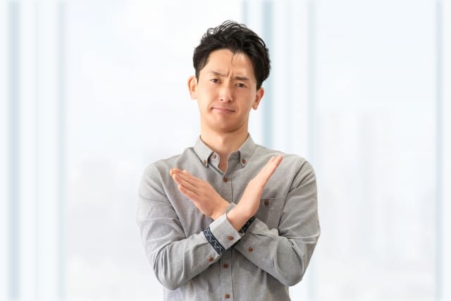 手でバツのポーズをする男性の画像