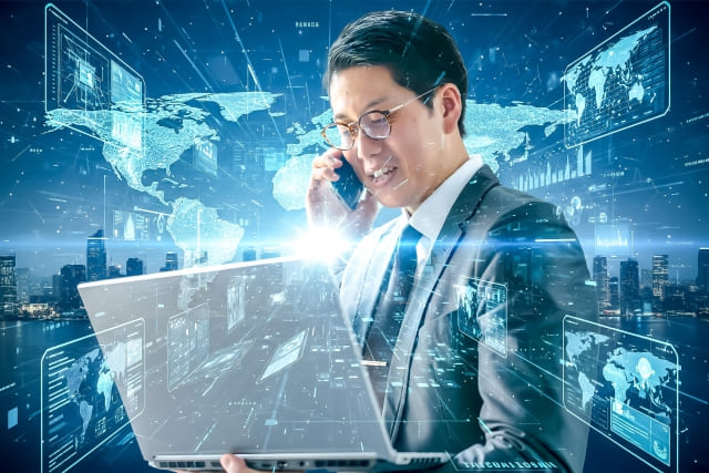 電話をしながらパソコンの画面を見ているビジネスマンの画像